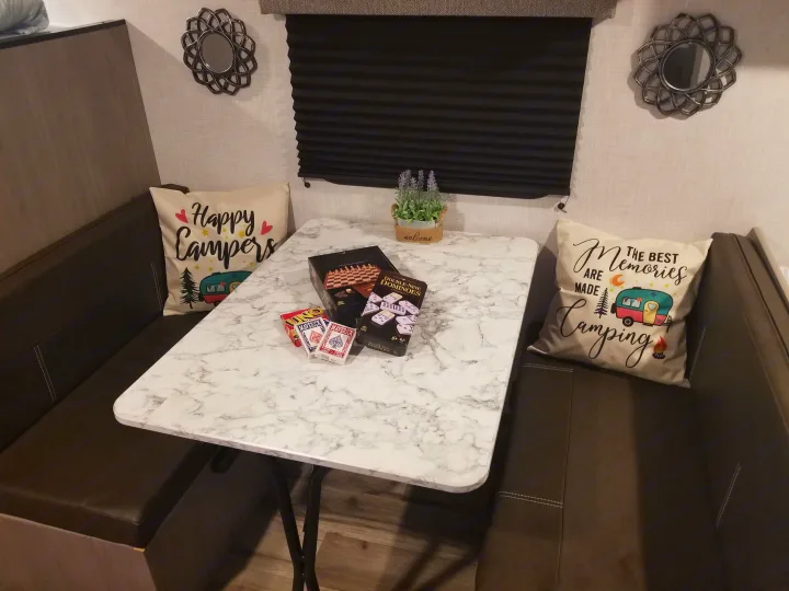 This RV rental dinette features comfy bench seating, a marble-look table with games (Uno, dominoes, chess), and charming camping pillows.. Coleman Lantern 17B 2023