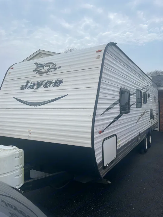 A white Jayco travel trailer, great for an rv rental, parked on a paved surface under a cloudy sky.. Jayco Jay Flight SLX 2017