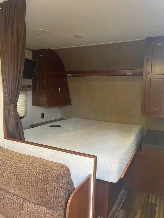A comfortable RV rental bedroom featuring a clean white bed, mounted TV, built-in storage, and earthy-toned decor.. Jayco Jay Flight SLX 2017
