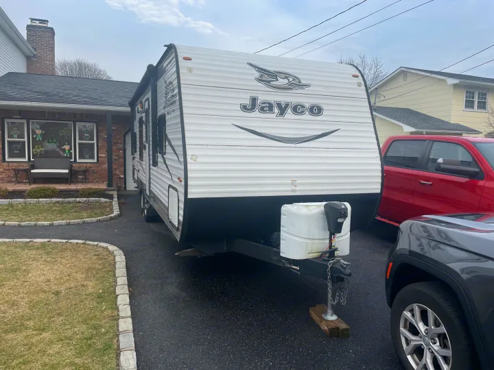 White Jayco travel trailer (RV rental) parked in a paved driveway beside a brick house with St. Patrick's Day window decorations.. Jayco Jay Flight SLX 2017