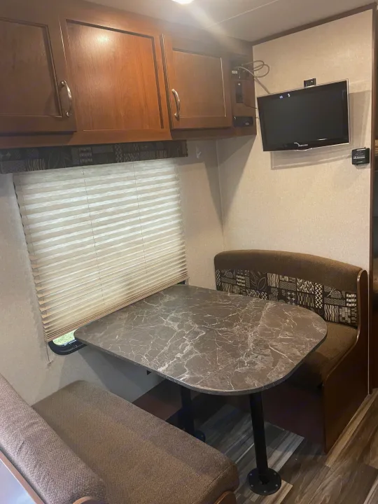 An RV rental features a comfortable dinette with a stone-look table, window blinds, storage cabinets, and a flat-screen TV.. Jayco Jay Flight SLX 2017