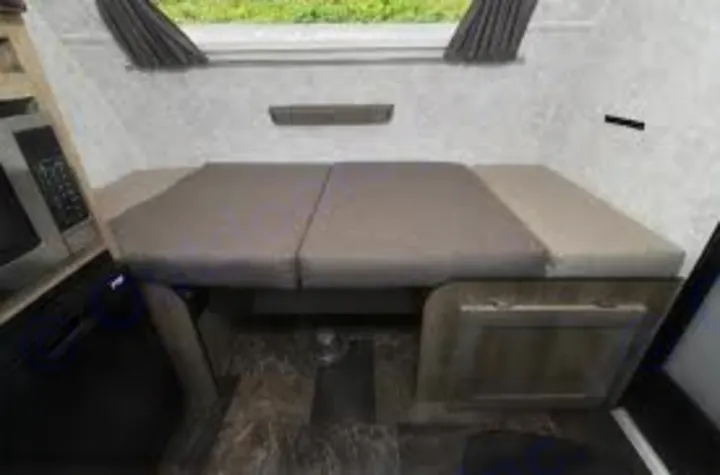 Inside this RV rental: A compact dinette with gray cushions converts to a cozy bed. Microwave and small fridge are on the left.. Prolite 12 V 2019