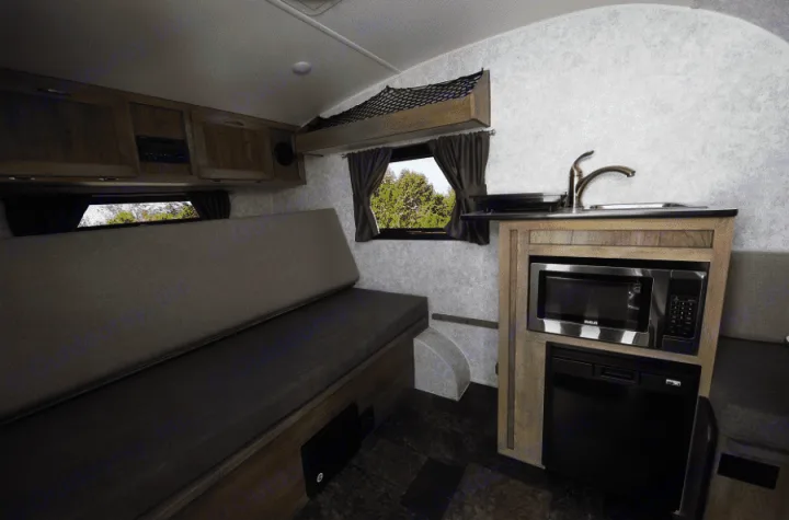 Compact RV rental interior with convertible bench seating, kitchenette (microwave, fridge, sink), and overhead storage.. Prolite 12 V 2019