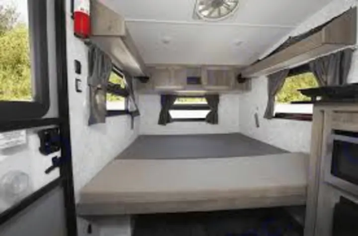 Step inside this RV rental! A compact camper interior with a large bed, overhead cabinets, and windows for your cozy travel adventures.. Prolite 12 V 2019