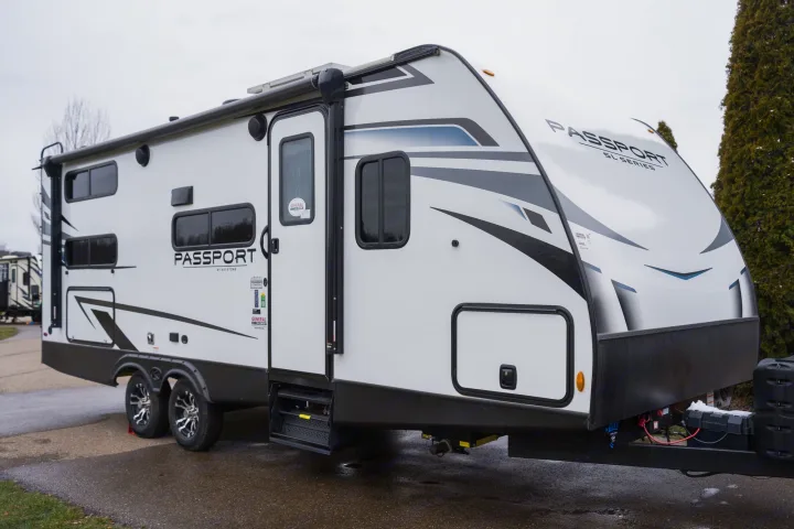 Side view of a white Keystone Passport SL Series travel trailer, ideal for an RV rental, parked on asphalt. Features dark windows & graphics.. Keystone RV Passport SL 2022