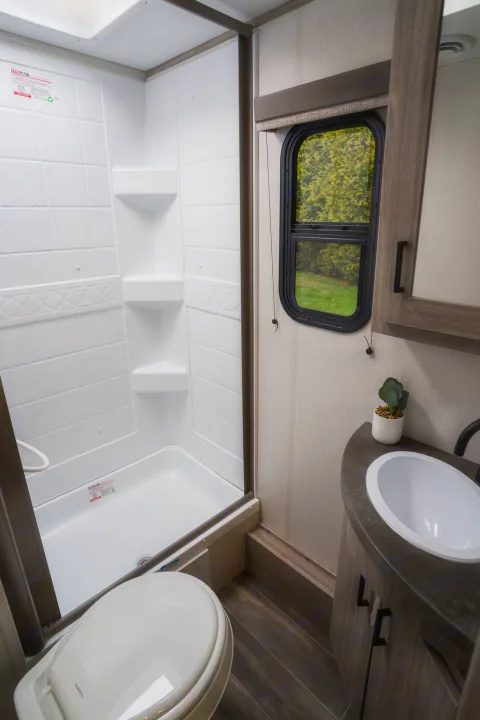 Compact **RV rental** bathroom with a white shower, toilet, and a sink vanity, ideal for travel.. Keystone RV Passport SL 2022