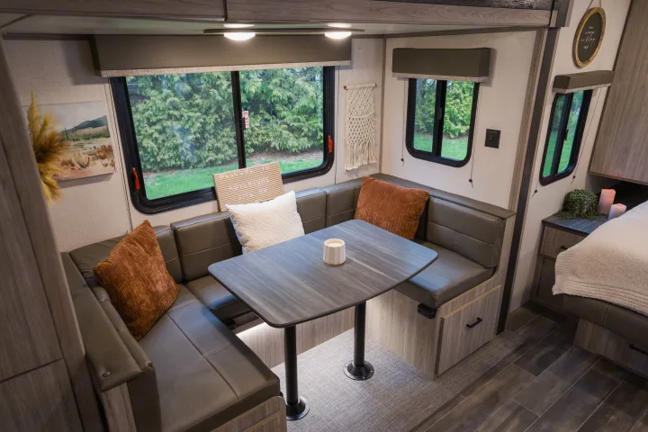 Cozy RV rental interior: a modern dinette with U-shaped seating, a table, and large windows revealing green trees.. Keystone RV Passport SL 2022
