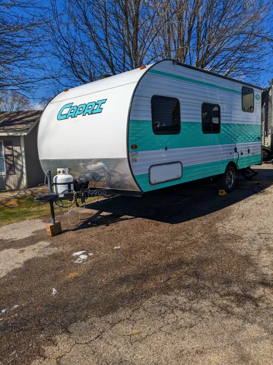 Explore with this vibrant white and teal Capri travel trailer RV rental, parked outdoors on a sunny day.. Gulf Stream Capri 2019