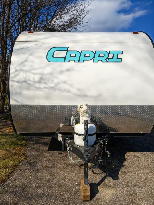 Front view of a white Capri travel trailer (RV rental option) with a propane tank, stuffed animal, and diamond plate trim.. Gulf Stream Capri 2019