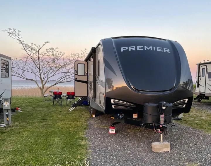 An RV rental, a dark Premier travel trailer, at a scenic waterfront campsite during sunset.. Keystone RV Bullet Premier Ultra 2020