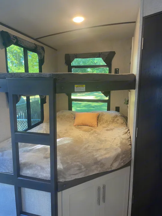 Inside this RV rental: cozy upper & lower bunk beds with plush bedding, bright windows, and cabinet storage.. Keystone RV Bullet Premier Ultra 2020