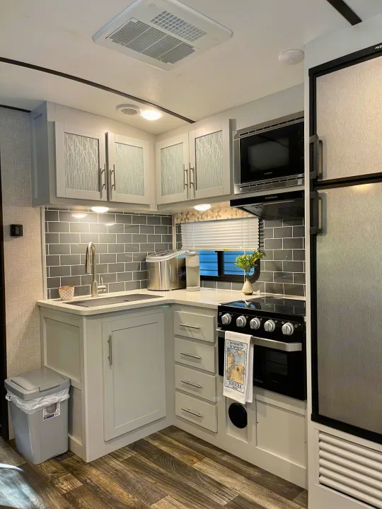 A well-appointed, modern RV rental kitchen showcasing grey cabinets, subway tile backsplash, and compact appliances.. Keystone RV Bullet Premier Ultra 2020