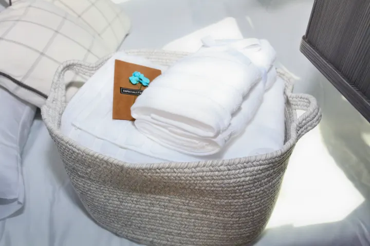 RV rental amenities: A woven basket holding fresh white towels and a welcome card on a cozy bed. Enjoy comfort on your trip.. Airstream Interstate 2021