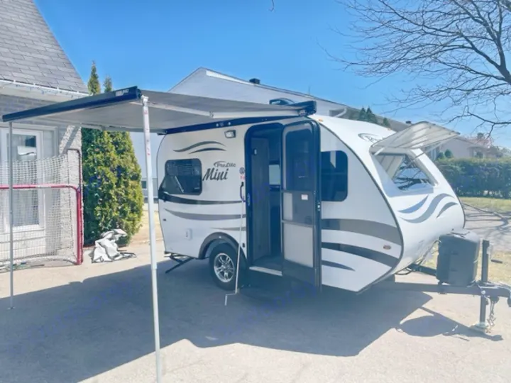 Compact white ProLite Mini travel trailer RV with its awning extended, parked outdoors. Great for your next rv rental.. Prolite Prolite Trailer 2022