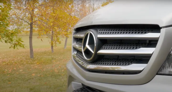 Front grille of a Mercedes-Benz van, ideal for rv rental adventures, against autumn trees.. Pleasure-Way Pleasure-Way Class B 2018