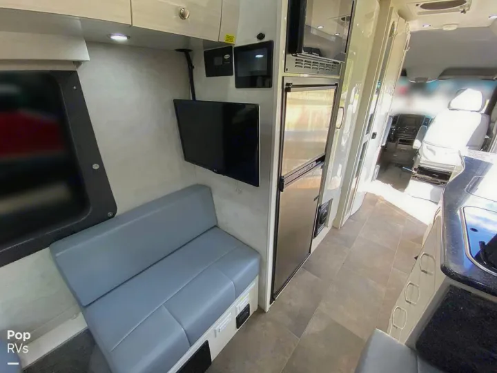Spacious RV rental interior with bench seating, TV, kitchenette (fridge/microwave), and driver's cabin view.. Pleasure-Way Pleasure-Way Class B 2018