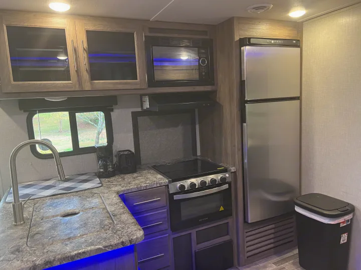 Modern RV rental kitchen with sink, microwave, stove, fridge, and blue accent lighting under overhead cabinets.. Crossroads RV Zinger 2022