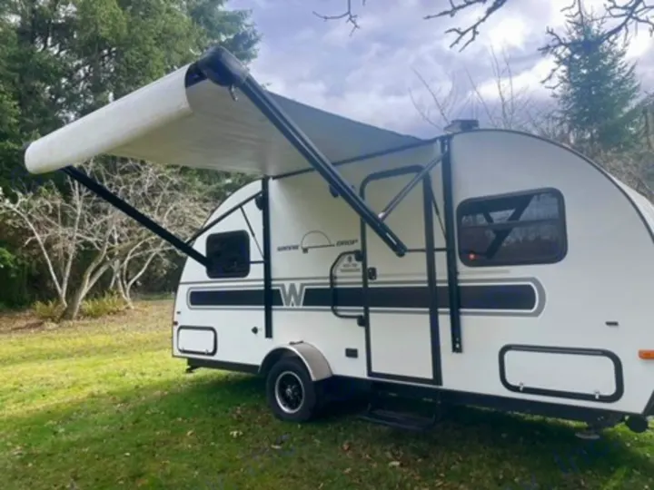 White teardrop camper with extended awning on grass. Ideal for an RV rental outdoor adventure.. Winnie Drop Winnie Drop Trailer 2017