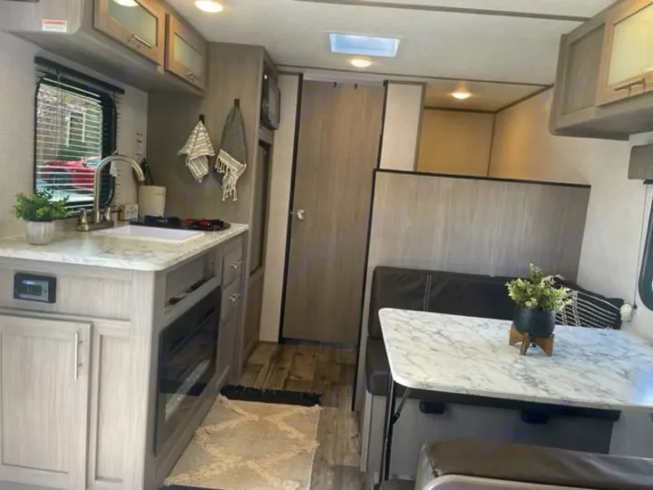 Bright, modern RV rental interior: kitchen with stove & sink, dining booth, light wood accents.. Dutchmen Coleman Lantern LT 2023
