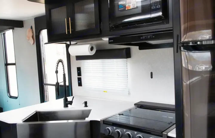 Modern RV rental kitchen featuring a stainless sink, black appliances, white counters, and stylish black cabinets with gold pulls.. Forest River Cherokee Grey Wolf 2022