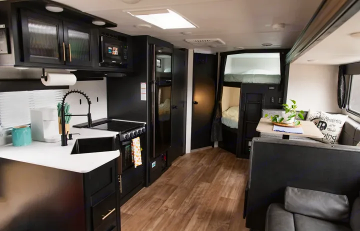 Modern RV rental interior: black kitchen, dining area, sofa, and cozy bunk beds for a comfortable stay.. Forest River Cherokee Grey Wolf 2022