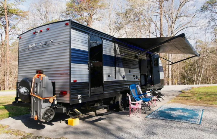 Grey Wolf travel trailer RV rental at a wooded campsite, with awning extended and outdoor seating area.. Forest River Cherokee Grey Wolf 2022
