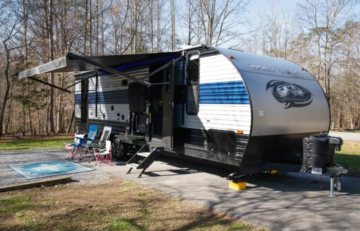 RV rental: A Grey Wolf travel trailer with extended awning, chairs, and rug at a wooded campsite.. Forest River Cherokee Grey Wolf 2022