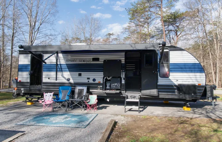 A spacious Grey Wolf travel trailer (RV rental) at a sunny campsite. Awning extended, doors open, with outdoor chairs and rug.. Forest River Cherokee Grey Wolf 2022