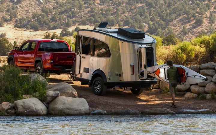 Red truck towing a travel trailer near a river, man with kayak. Perfect for an RV rental adventure!. Airstream Basecamp 2020