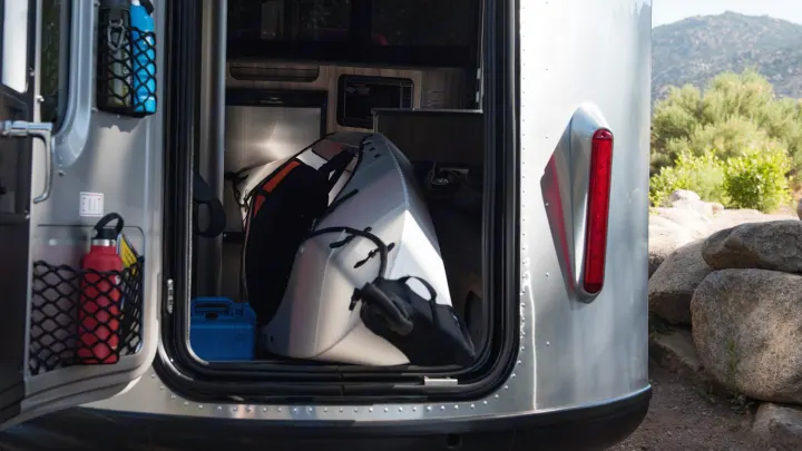 The rear hatch of a silver RV rental is open, revealing a folded kayak and gear storage inside, perfect for outdoor adventures.. Airstream Basecamp 2020