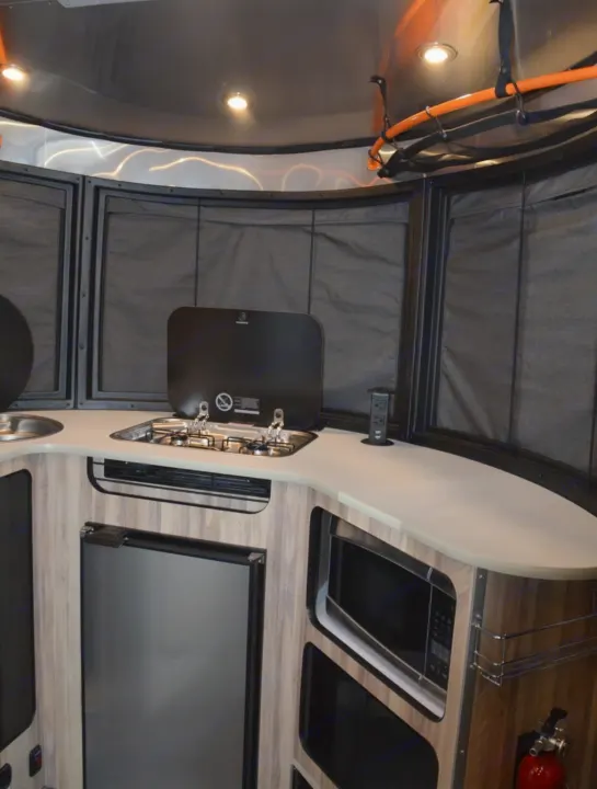 This RV rental kitchen boasts a stove, sink, fridge, microwave, and counter space, ideal for travel cooking.. Airstream Basecamp 2020