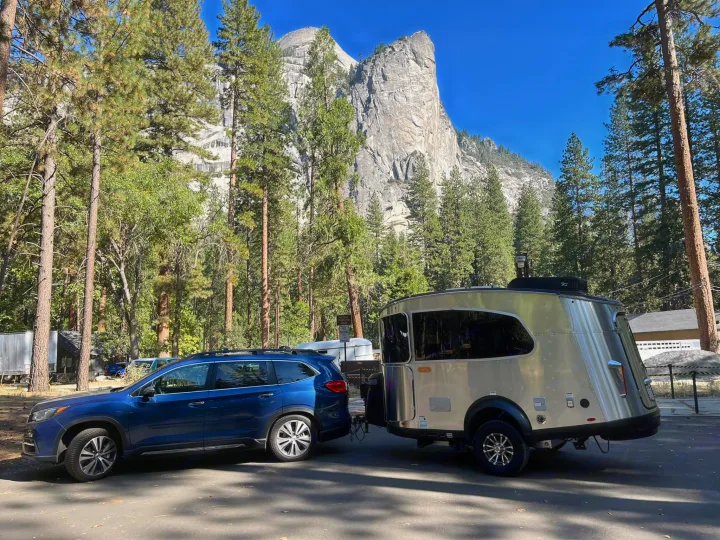Yosemite adventure: Blue SUV towing a silver rv rental travel trailer, with Half Dome & El Capitan towering above.. Airstream Basecamp 2020