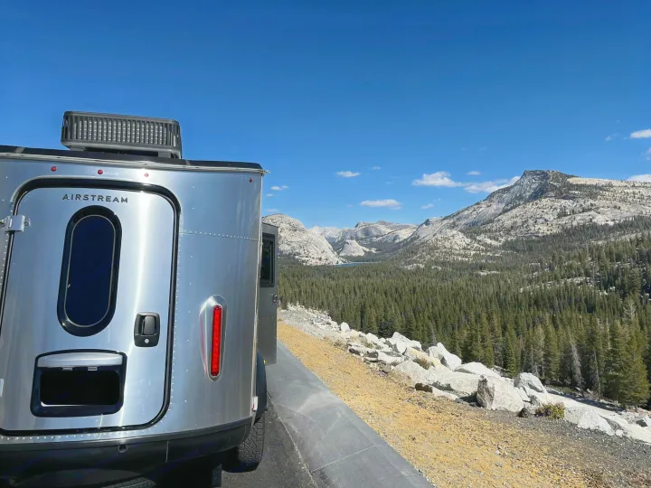 Airstream RV rental parked at a scenic mountain overlook, showcasing a vast forest and distant lake under a clear sky.. Airstream Basecamp 2020