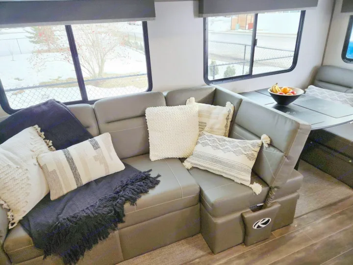 Spacious RV rental interior: comfortable sectional sofa, dinette with fruit bowl, and snowy window views.. Keystone RV Passport GT 2022