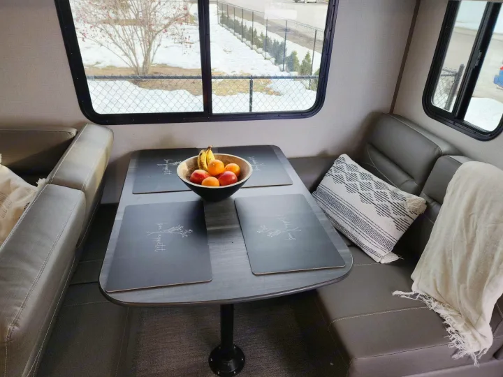 Cozy RV rental dinette with a fruit bowl on the table, comfortable bench seating, and a large window showcasing a snowy landscape.. Keystone RV Passport GT 2022