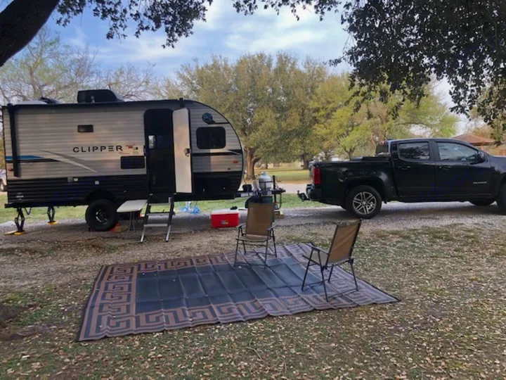 Travel trailer RV rental parked at a serene campsite with a truck, outdoor mat, and chairs. Ready for adventure.. Forest River Coachmen RV Clipper Ultra-Lite 17BH 2022