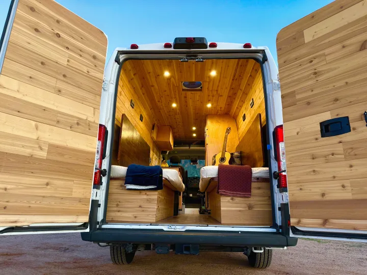 Cozy wood interior of a custom camper van, perfect for RV rental adventures, featuring beds, a guitar, and warm lighting.. Custom Promaster 2021 2021