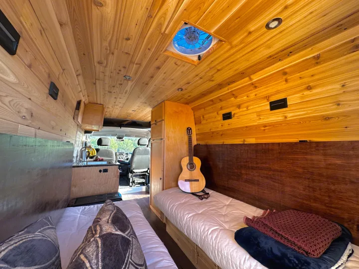 Spacious RV rental interior with custom wood finishes, dual beds, and a functional kitchen, perfect for mobile living.. Custom Promaster 2021 2021