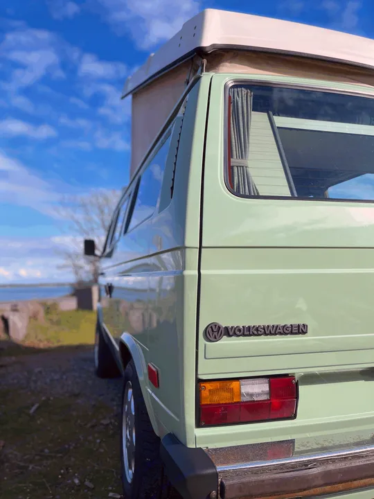 A mint green pop-top VW camper van by the water, perfect for your next RV rental adventure!. Volkswagen T3 Westfalia 1986