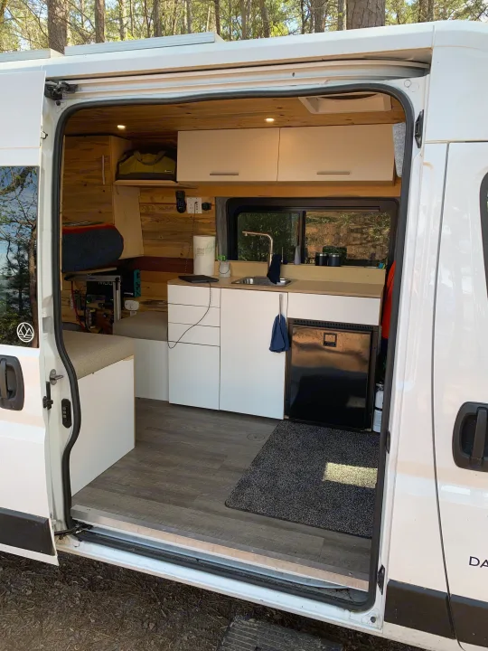 Spacious RV rental interior showcasing a custom-built kitchen, sleeping area, and storage with wood accents and white cabinets.. Dodge Sprinter Van 2020
