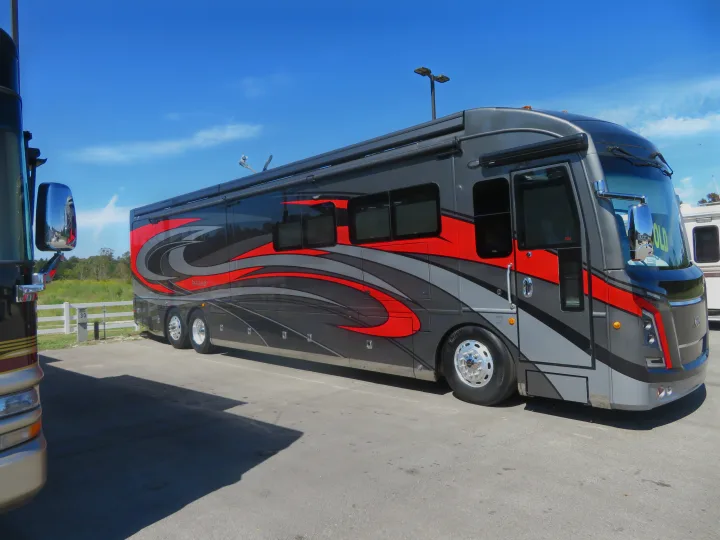 A sleek black, gray, and red RV, perfect for an RV rental adventure, parked on asphalt under a clear blue sky.. Monaco Signature 2019