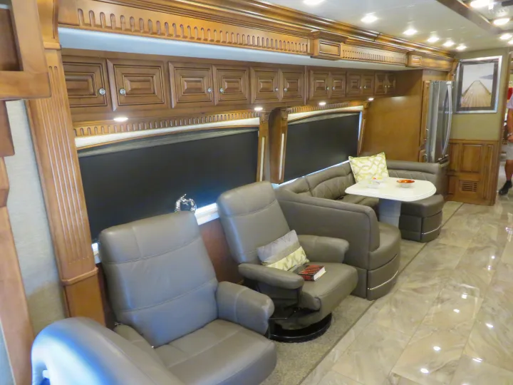 Inside a premium RV rental: comfortable leather recliners, a dining booth, and overhead wood cabinetry create a luxurious space.. Monaco Signature 2019