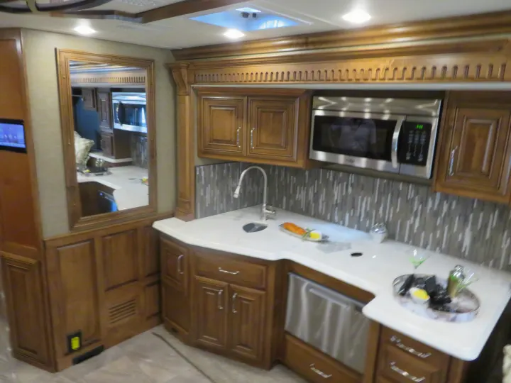 Luxurious RV rental kitchen features wood cabinets, microwave, sink, and stylish white counters. Ideal for comfortable travel.. Monaco Signature 2019