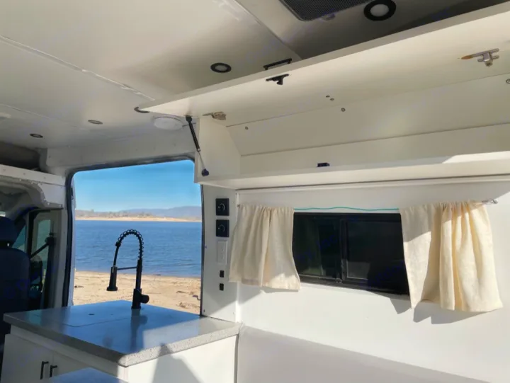 RV rental ready for adventure: white camper van interior with kitchen, overhead storage, and scenic lake & mountain view.. Dodge RAM Promaster 2500 2019
