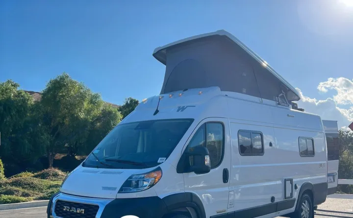 White Ram camper van with a raised pop-top roof, parked outdoors under a bright blue sky. Ideal for rv rental adventures.. Winnebago Solis 2023