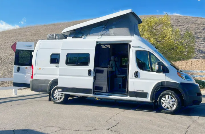 White Winnebago Solis rv rental with extended pop-top and open side/rear doors, showcasing its interior.. Winnebago Solis 2023