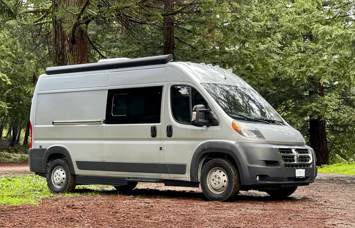 This spacious light gray RV rental camper van is parked on a forest trail, ready for your next nature road trip.. Hymer Sunlight Van 1 2018