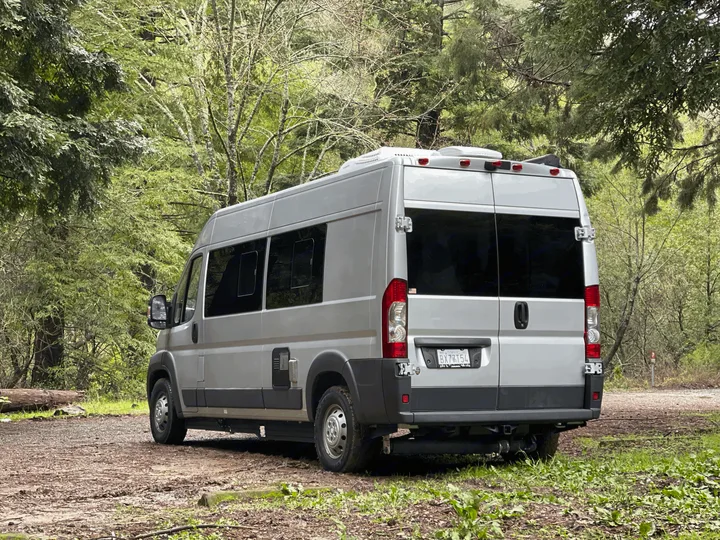 Silver RV rental camper van parked on a dirt path amidst lush forest. Ideal for nature and outdoor adventures.. Hymer Sunlight Van 1 2018
