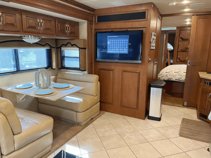 An RV rental's inviting living area with a dining table, entertainment system, and access to the bedroom.. Fleetwood Discovery 2011