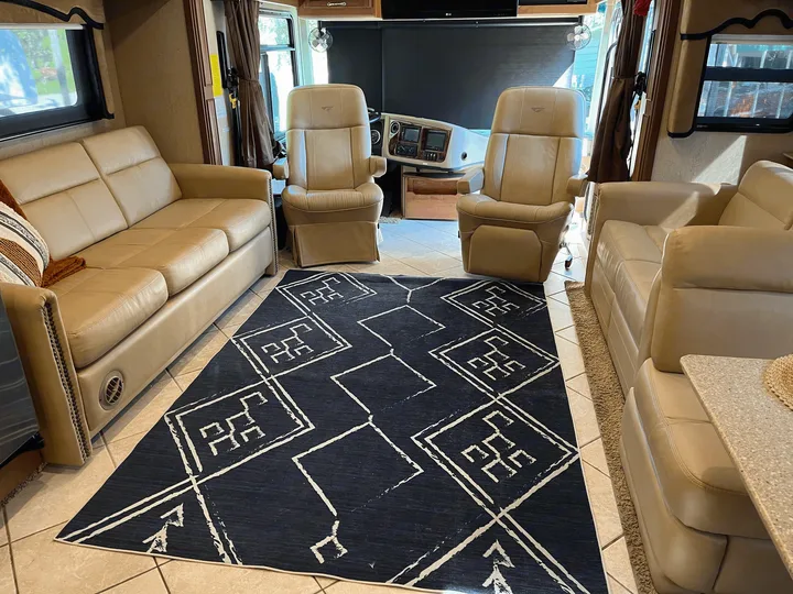 Modern RV rental living area featuring beige leather sofas, captain's chairs, and a blue geometric rug.. Fleetwood Discovery 2011
